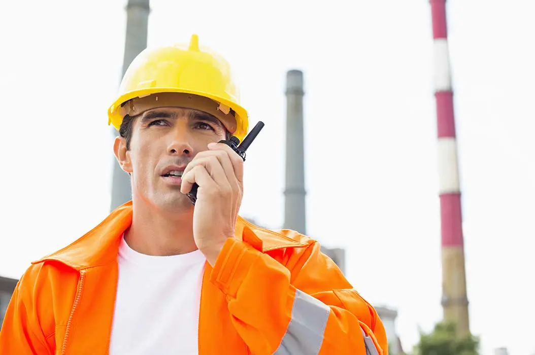 Man-on-radio-in-hardhat-and-overalls-infront-of-towers